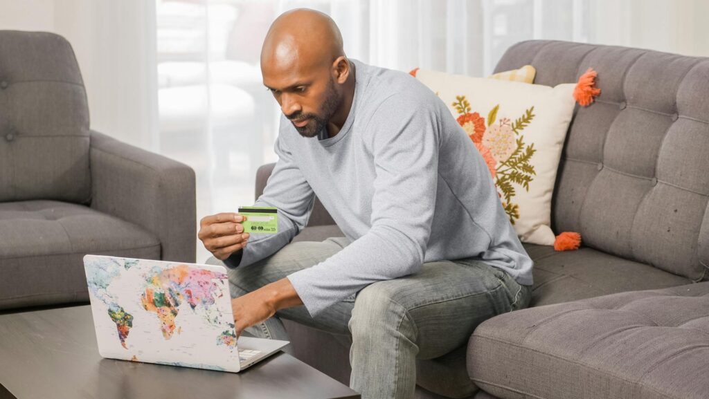 Man sitting on couch in front of laptop and holding up gift card