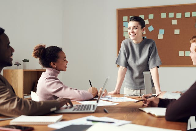 A worker standing at the edge of a table discussing channel incentive management with co-workers